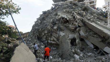 Pessoas caminham para resgatar os escombros de um prédio desabado em Lagos, Nigéria. 