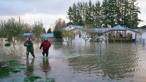 As irmãs Miranda, à esquerda, e Christine Archer caminham através das enchentes saindo da casa de seu tio, na segunda-feira, 15 de novembro de 2021, em Sedro Woolley, Washington.  (AP Photo / Elaine Thompson)