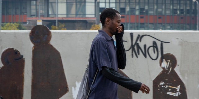 Um homem usa a mão para cobrir o nariz enquanto caminha em uma rua no centro de Joanesburgo, na África do Sul, na segunda-feira, 16 de março de 2020.
