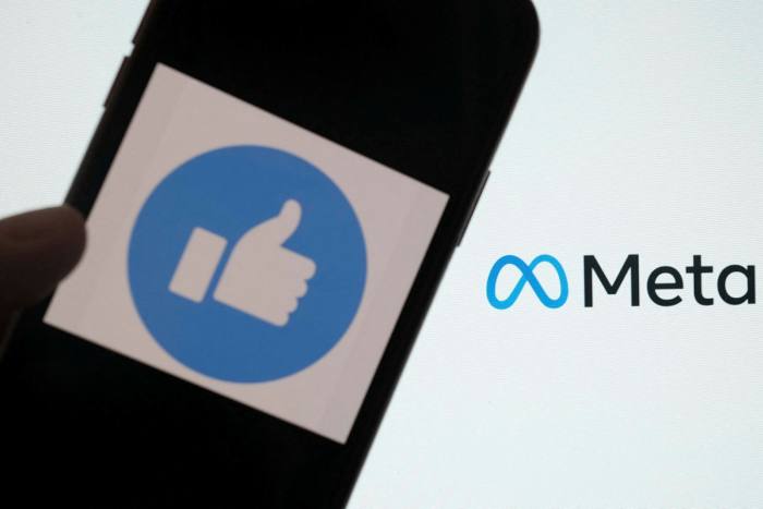 Uma pessoa usa o Facebook em um smartphone na frente de uma tela de computador mostrando o logotipo Meta