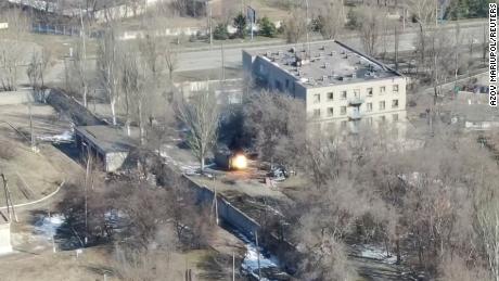 Esta captura de tela de imagens de drones mostra um veículo militar disparando tiros perto de um prédio.