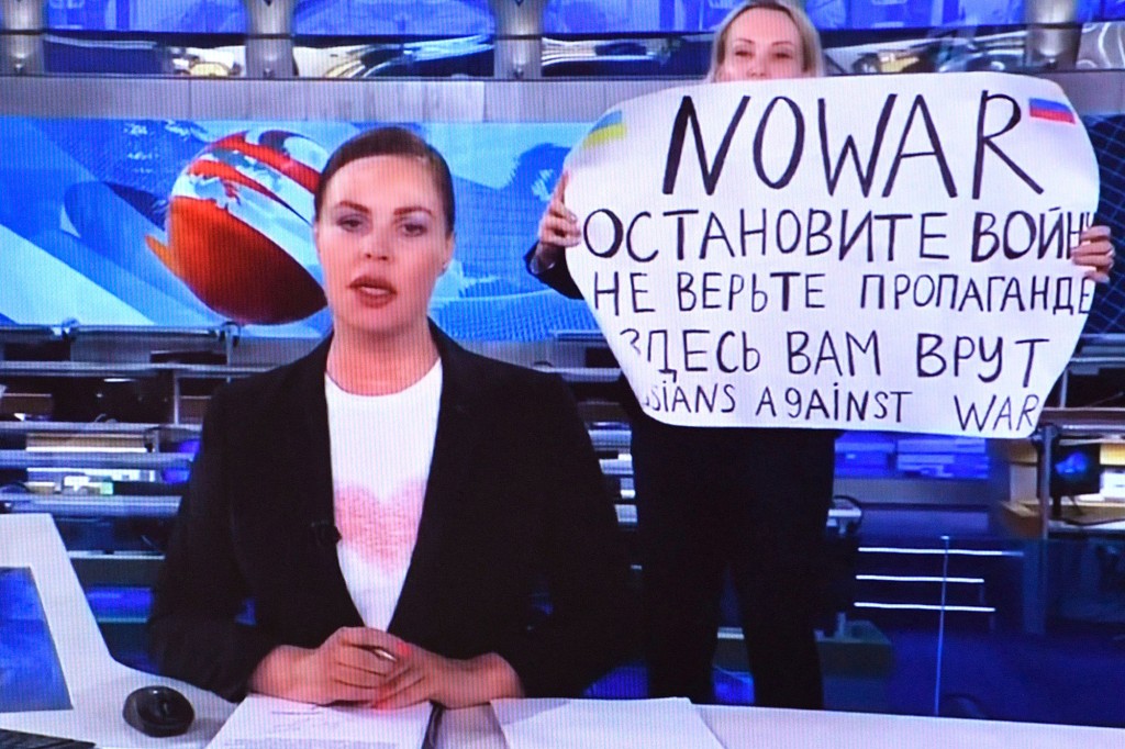 Uma mulher olha para uma tela de computador assistindo um funcionário dissidente russo do Channel One entrar no estúdio de TV Ostankino ao vivo durante a transmissão do noticiário noturno mais assistido na Rússia.