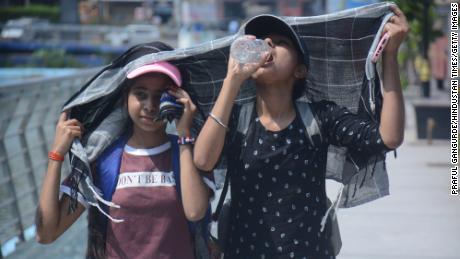 As meninas cobrem a cabeça enquanto caminham e bebem água no calor escaldante da tarde de Mumbai.
