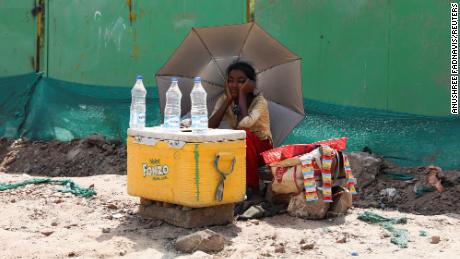 Uma garota que vende água usa um guarda-chuva para se proteger dos raios do sol em Nova Délhi.