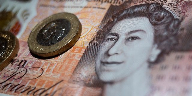 Moeda britânica de duas libras colocada em cima de uma nota de 10 libras do Banco da Inglaterra com o retrato da rainha Elizabeth II.