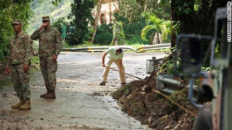 A Guarda Nacional força o trânsito enquanto o residente Luis Nogueira ajuda a limpar uma estrada danificada pelo furacão Fiona em Cayai, Porto Rico, na terça-feira.